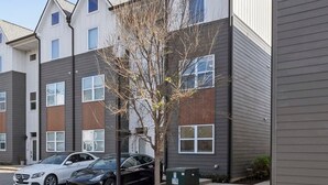 Un edificio residencial de varios pisos con estacionamiento, un árbol y cielo despejado.