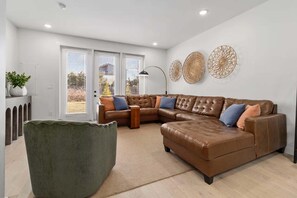Un salon moderne avec un canapé d’angle en cuir marron, un fauteuil vert et des œuvres d’art décoratives accrochées au mur.