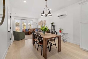A dining area with a wooden table and chairs, a hanging light fixture, and a view of the living room through glass doors. - Lookout Living 1405–Downtown Access–Sleeps 8 (Chattanooga)