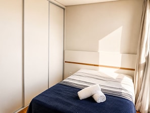 Un dormitorio con cama, armario y ventana con cortinas.