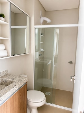 Un baño con ducha de vidrio, inodoro blanco, encimera de granito y espejo sobre el lavabo.