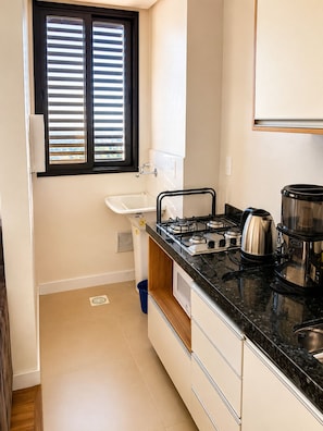 Una cocina compacta con estufa a gas, cafetera y ventana con persianas.