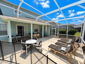 Ein überdachter Patio-Bereich mit Gartenmöbeln, einem Tisch und einem Gewächshaus.