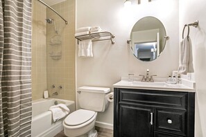 Un baño con bañera, inodoro y tocador con espejo.