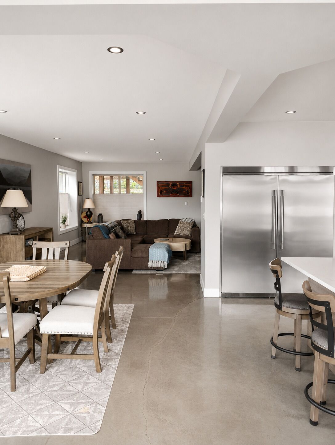 Una cocina moderna con un refrigerador de acero inoxidable, un comedor con mesa y sillas de madera, y una sala de estar con sofá y una mesa de centro.