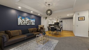 A modern living room with a dark blue accent wall, a brown leather sofa, a coffee table, and a patterned rug. - Central Peaks Retreat - walk to CBD (Queenstown)