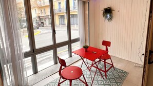 Ein Zimmer mit einem großen Fenster, einem roten Tisch mit Stühlen, einem gemusterten Teppich und einer hängenden Leuchte.