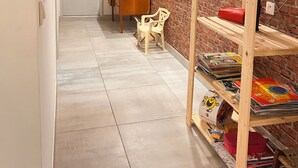 Ein Korridor mit Backsteinwand, einem Holzregal mit Büchern, einem Tisch mit Stühlen und einer Tür.