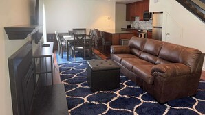 A living room with a brown leather sofa, a TV, a dining table with chairs, and a kitchen in the background. - Tahoe Pines Escape (Incline Village)