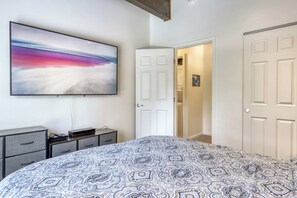 Une chambre à coucher avec un grand lit, un téléviseur à écran plat fixé au mur, une commode et une porte donnant sur un placard.