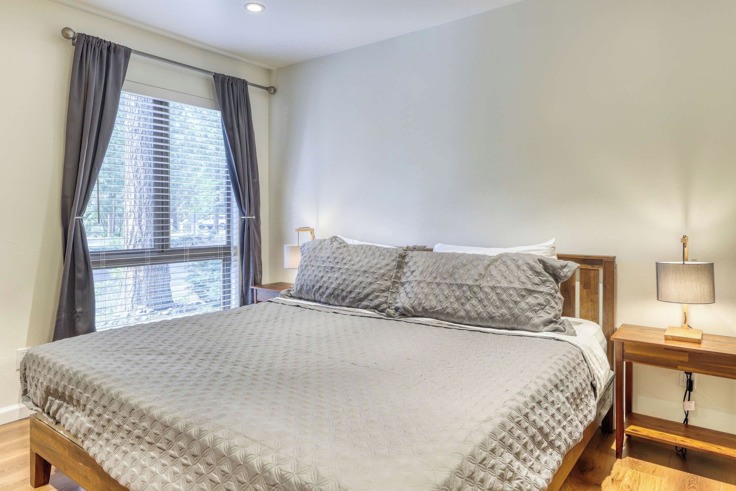 Une chambre à coucher avec un lit, une table de chevet, une lampe et une fenêtre avec des rideaux.