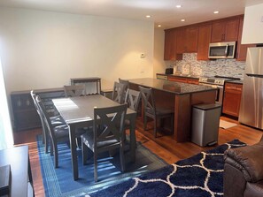 A modern kitchen with wooden cabinets, stainless steel appliances, a dining area with a glass table, and a patterned rug. - Tahoe Pines Hideaway (Incline Village)