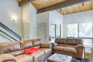 Ein Wohnzimmer mit einem Ledersofa, einem Ledersessel, einem kleinen Hocker und einem Fenster mit Jalousien.