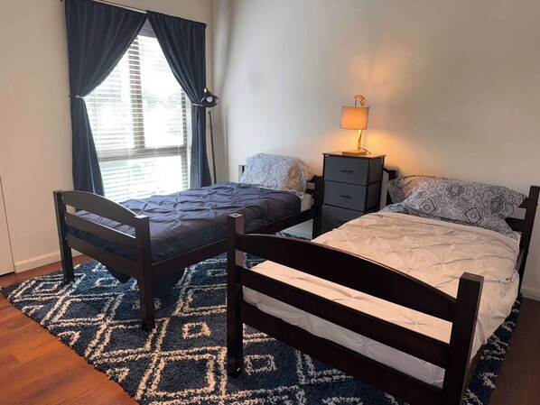A bedroom with two beds, a nightstand, a lamp, and a window with curtains. - Tahoe Pines Hideaway (Incline Village)