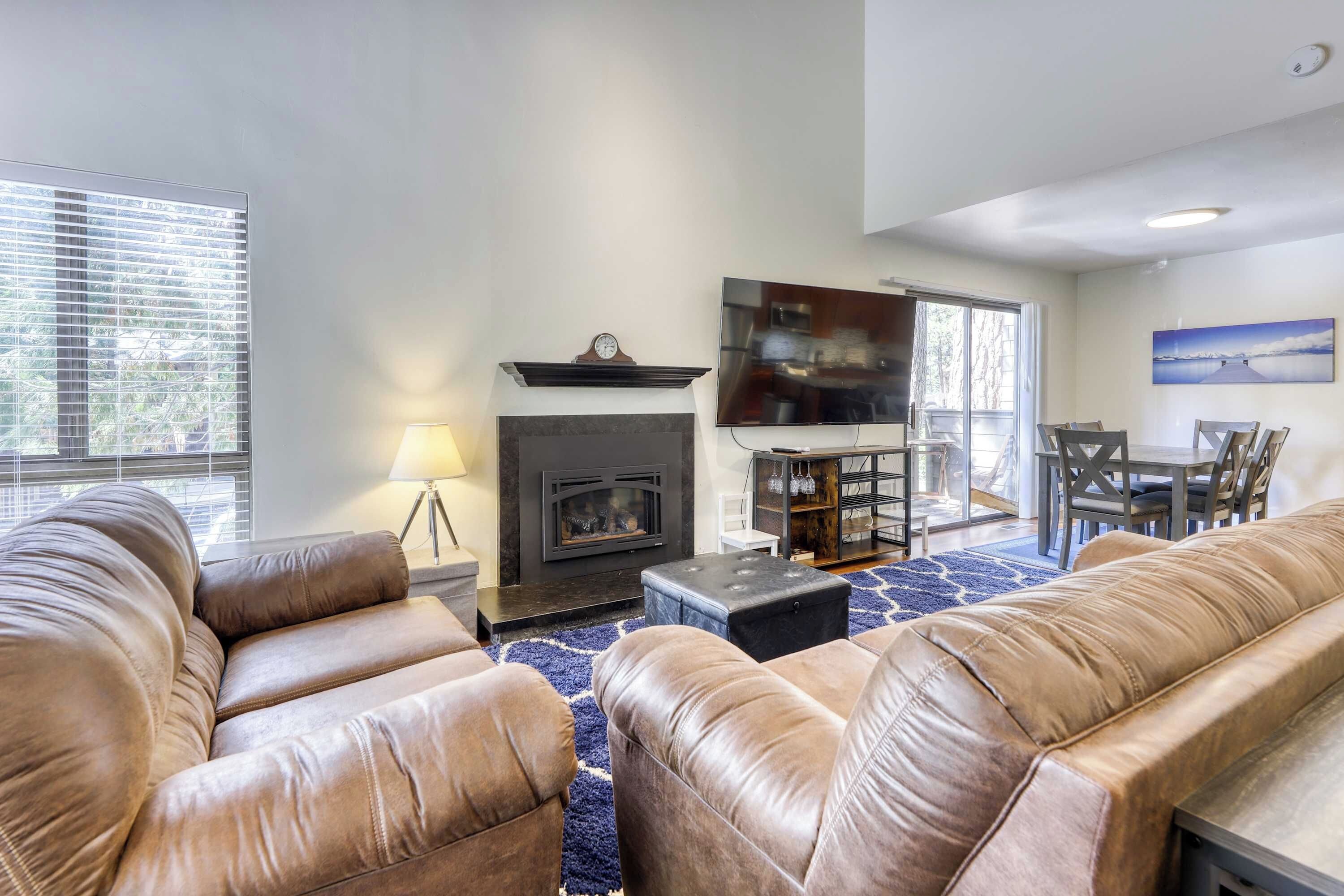 A living room with leather sofas, a fireplace, a dining area with a table and chairs, and a large window with blinds.