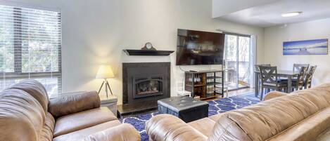 A living room with leather sofas, a fireplace, a dining area with a table and chairs, and a large window with blinds.