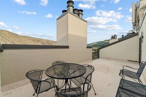 Una terrazza esterna con un tavolo rotondo e sedie, un camino e vista sulle colline.