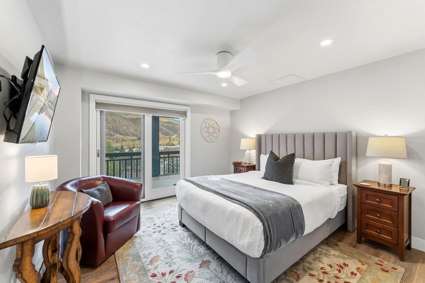 A hotel room with a bed, a desk, a chair, a nightstand, a lamp, and a view of the outdoors.