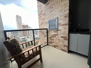 Un balcon donnant sur un paysage urbain, un banc en bois, un coin cuisine et un tableau encadré au mur.