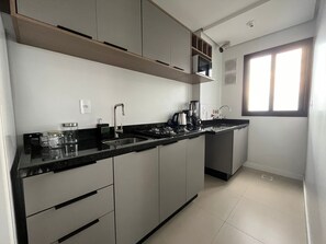 Une cuisine moderne dotée d’un plan de travail noir, d’appareils électroménagers en acier inoxydable et d’une fenêtre laissant entrer la lumière naturelle.