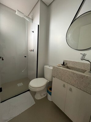 Un baño con ducha envuelta en vidrio, inodoro, lavamanos con encimera de granito y espejo.