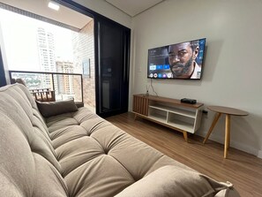 Una sala de estar moderna con sofá, televisor, mueble de televisión de madera y una pequeña mesa.