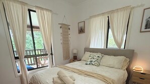 A bedroom with a large bed, two bedside tables, a hanging macrame wall decoration, and a window with curtains. - BROOMS HEAD PET FRIENDLY BEACH PAD with authentic retro arcade games machine. 🐶 (Brooms Head)