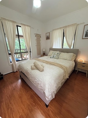 A bedroom with a large bed, two bedside tables, a hanging macrame wall decoration, and a window with curtains.