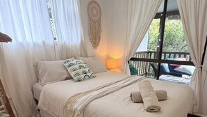 A bedroom with a bed, curtains, a wall hanging, and a window with a view. - BROOMS HEAD PET FRIENDLY BEACH PAD with authentic retro arcade games machine. 🐶 (Brooms Head)