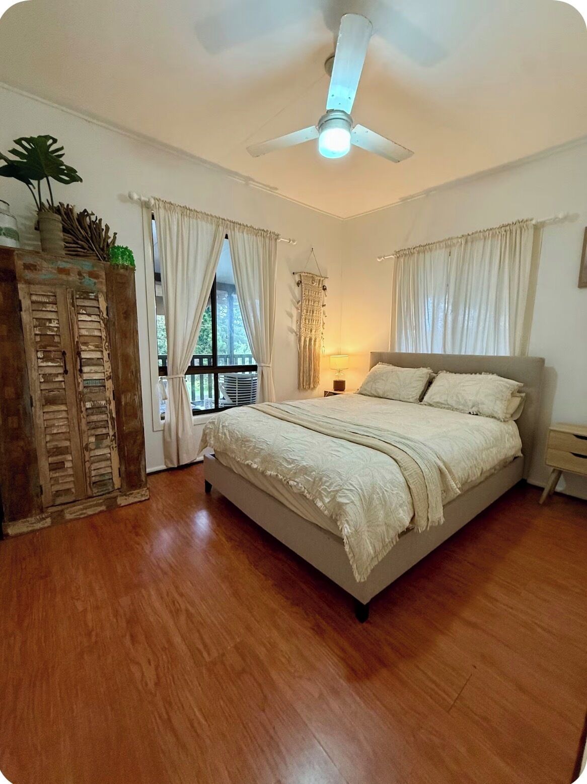 Une chambre à coucher avec un lit, un ventilateur de plafond et une fenêtre avec des rideaux.