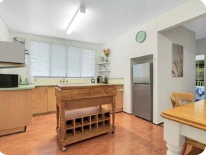 A kitchen with wooden cabinets, a stainless steel refrigerator, a wooden table, and a window with blinds.