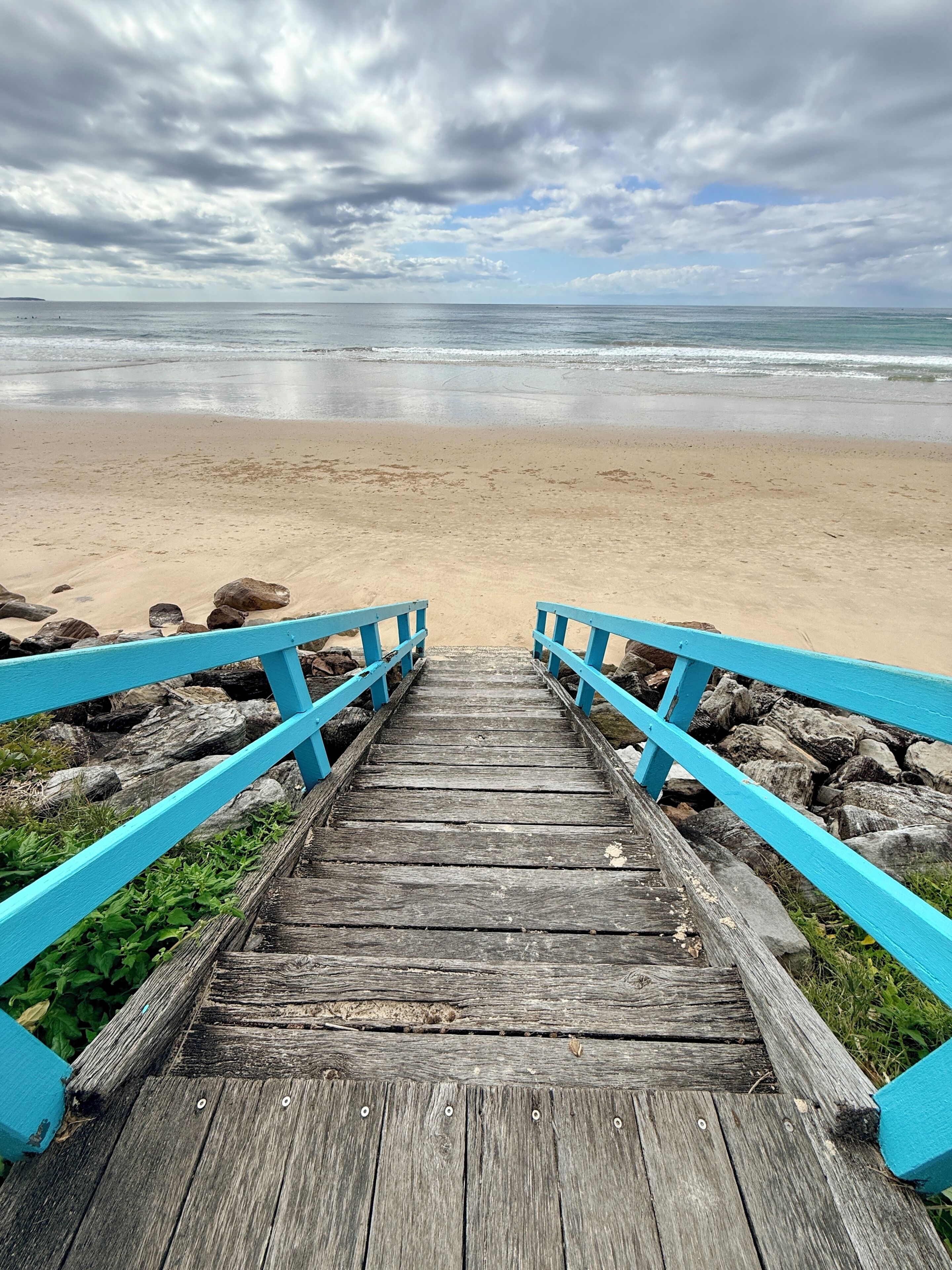 A wooden staircase leading to a beach with a cloudy sky.