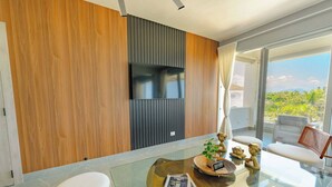 A modern living room with a flat-screen TV, a glass coffee table, and a balcony with a view.