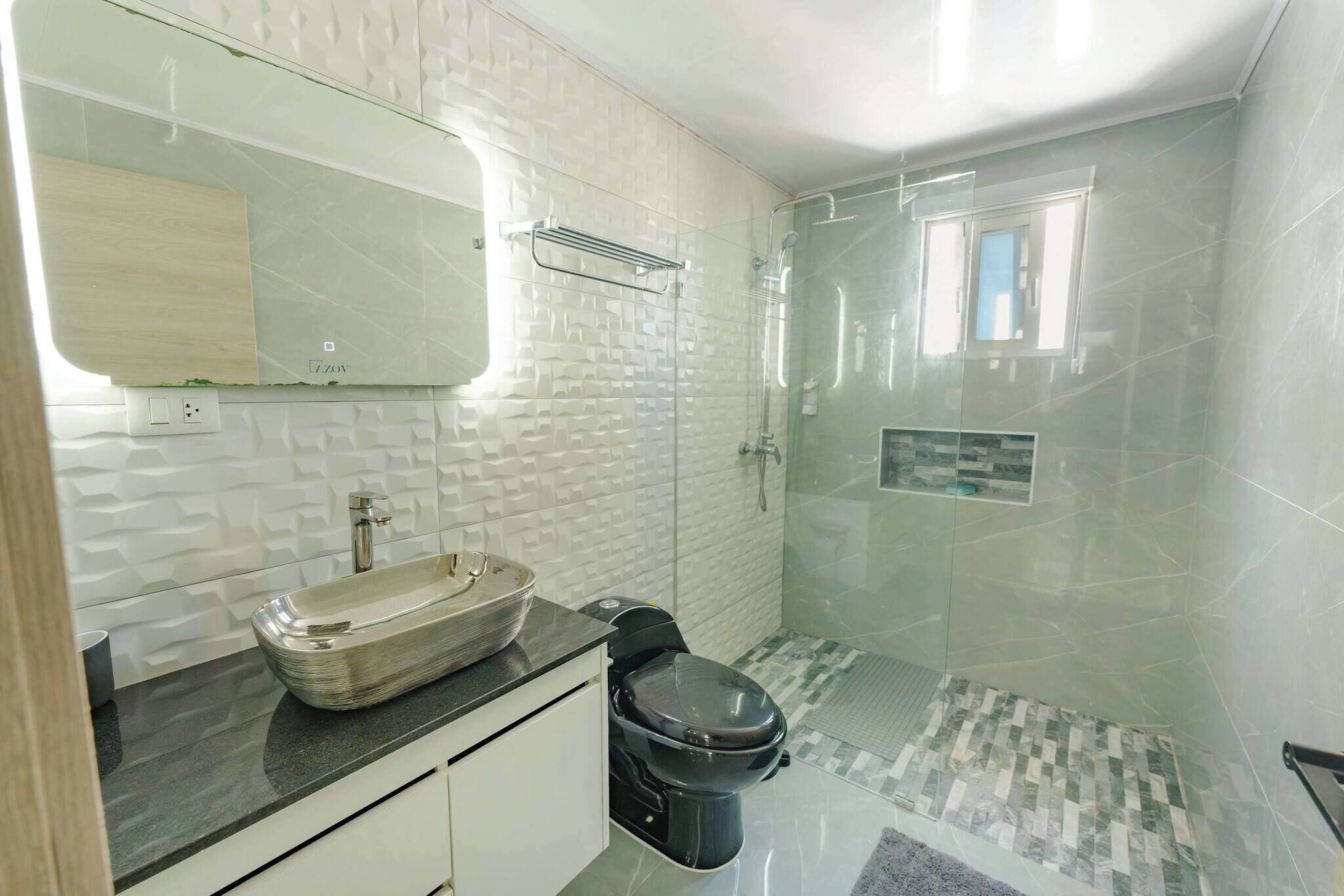 A bathroom with a glass shower enclosure, a sink with a vessel basin, and a toilet.
