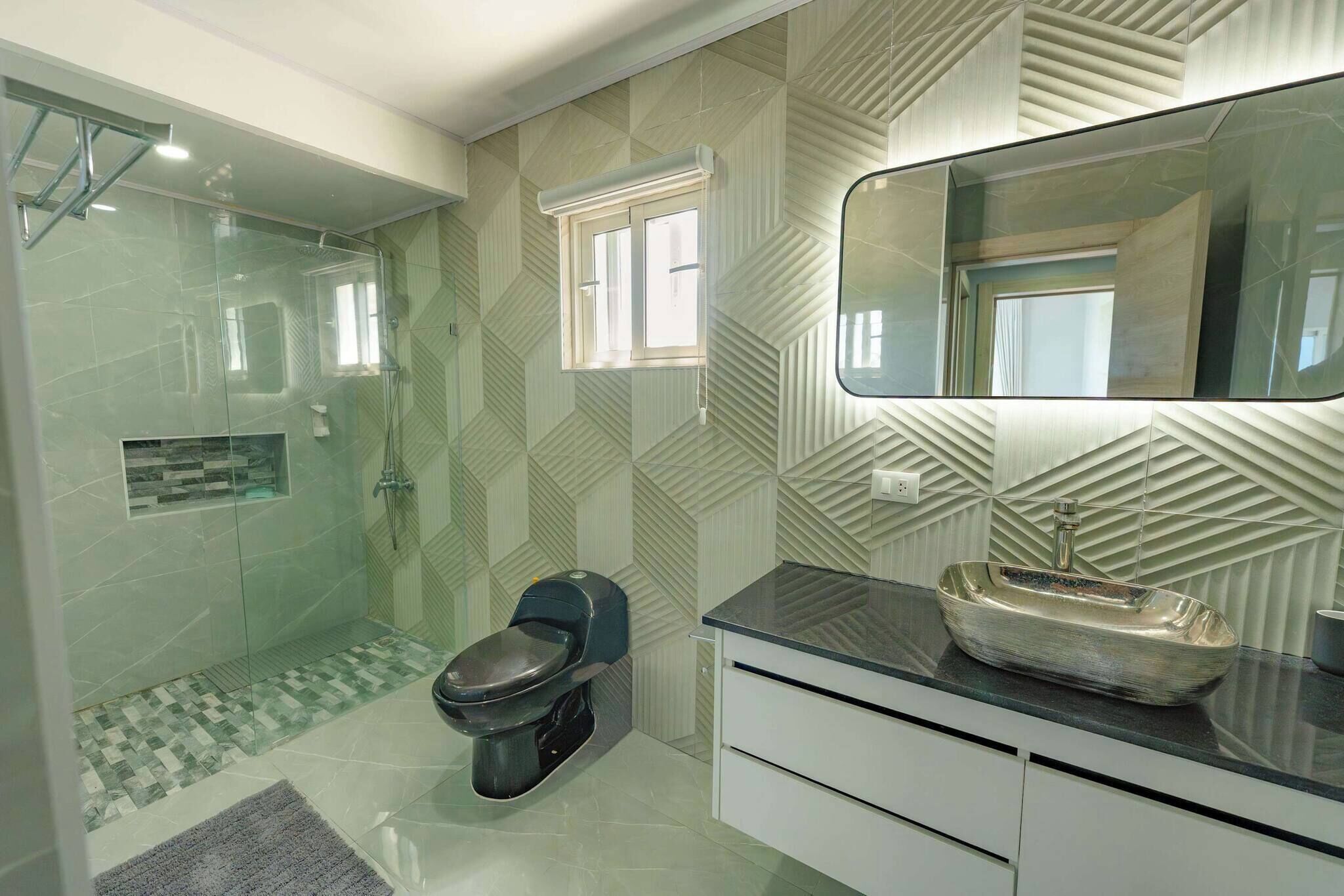 Un baño con ducha envuelta en vidrio, un inodoro, un lavabo con pila y un espejo sobre el lavabo.