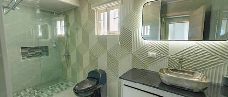 Un baño con ducha envuelta en vidrio, un inodoro, un lavabo con pila y un espejo sobre el lavabo.