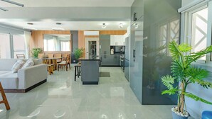 A modern kitchen with a central island, a dining area with a sofa and chairs, and a large window providing natural light.