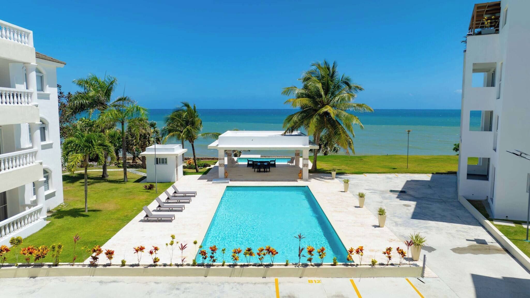 A pool with lounge chairs, a covered seating area, and a view of the ocean.