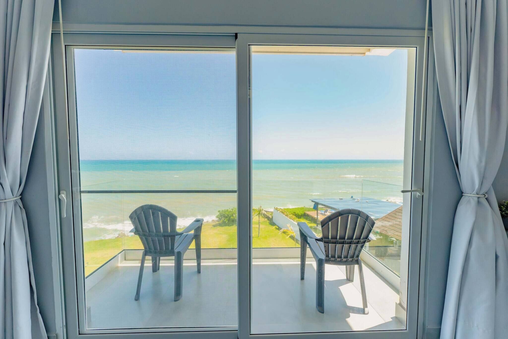 Ein Balkon mit zwei Stühlen und einem Tisch, der Blick auf einen Strand und das Meer bietet.