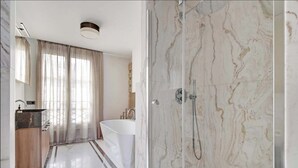 Ein modernes Badezimmer mit einer freistehenden Badewanne, einer gläsernen Duschkabine und einem Marmorboden.