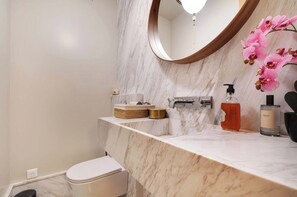 Ein Badezimmer mit Marmorplatte, Toilette, Waschbecken mit modernem Wasserhahn und Spiegel mit Holzrahmen.