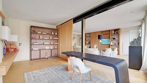 Ein modernes Wohnzimmer mit einem Holzregal, einem schwarzen Esstisch und einem weißen Sessel.