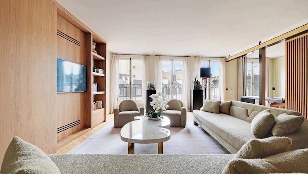 Ein modernes Wohnzimmer mit einer Couch, Sesseln, einem Couchtisch und einem Bücherregal.