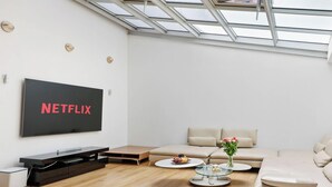 Een moderne woonkamer met een grote flatscreen televisie, een bank, een salontafel en een glazen tafel met bloemen.