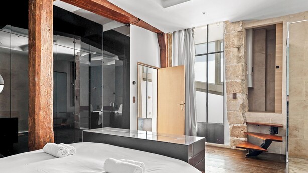 Een moderne hotelkamer met een groot bed, een houten pilaar, een spiegel en uitzicht op het exterieur.