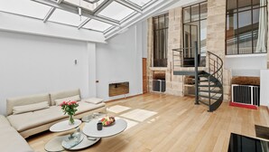 Een ruime woonkamer met een hoge plafond, een moderne trap en een groot raam.