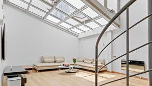Een moderne woonkamer met een groot raam, een bank, een salontafel en een aan de muur bevestigde televisie.