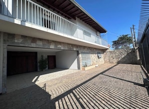 Un edificio de dos pisos con balcón, una pared de piedra y un camino de entrada pavimentado.
