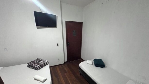 A small, single-room hotel room with two beds, a television mounted on the wall, and a door. - Hospedaria Campinas  (Campinas)