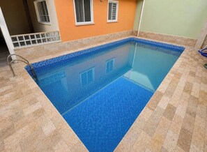 Una piscina rectangular con borde de azulejos, rodeada de piso y paredes alicatados.